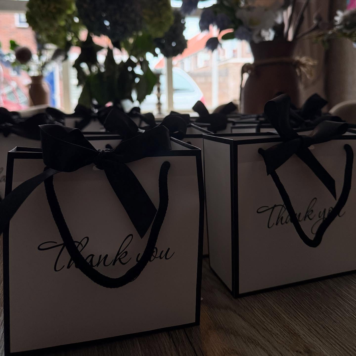Crèmekleurige goodiebags met zwarte strikken bij het raam